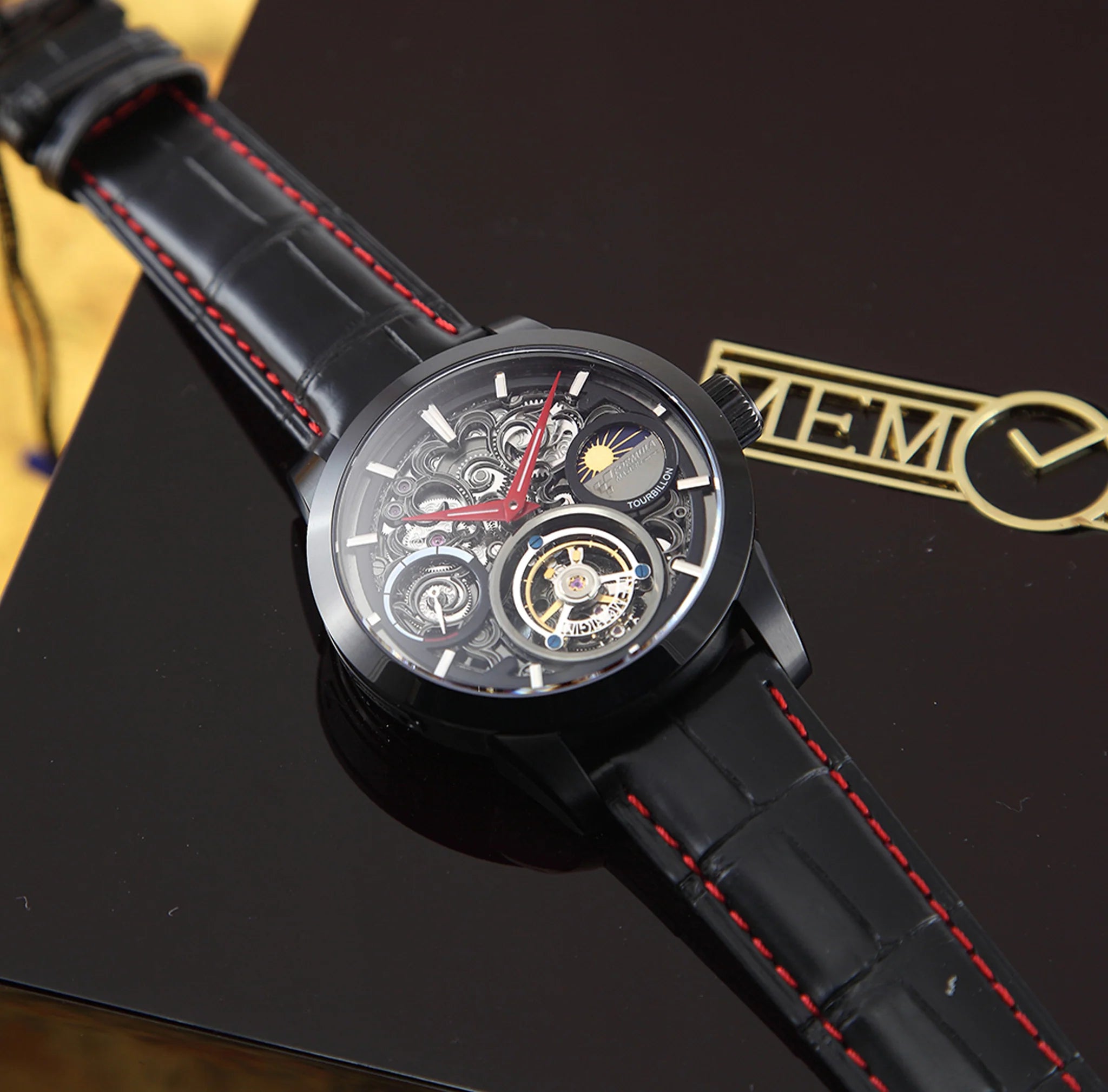 Black wristwatch with red stitching on a dark surface, featuring a brand logo.