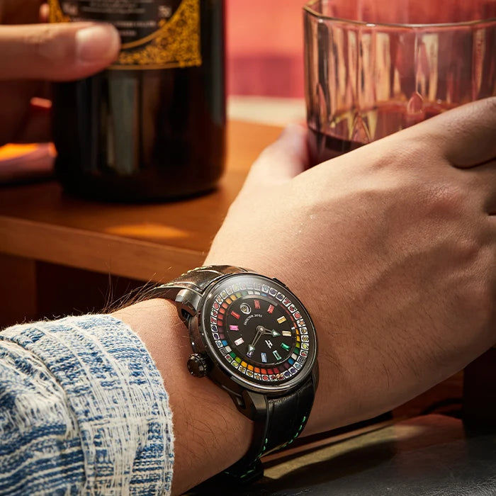 Person wearing a smartwatch with a colorful display, holding a glass and bottle on a wooden table.