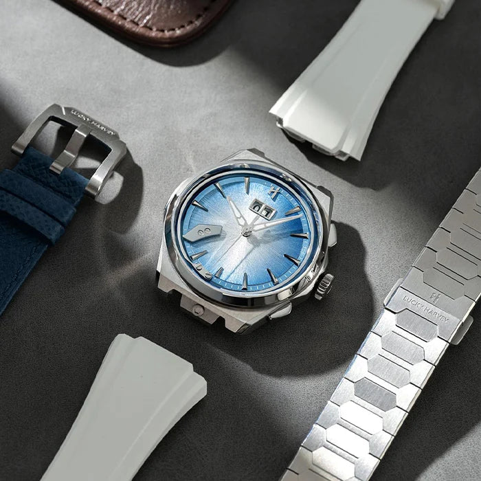 A silver-toned wristwatch with a blue sunburst dial and date window, styled on a dark gray surface with multiple interchangeable watch straps around it.