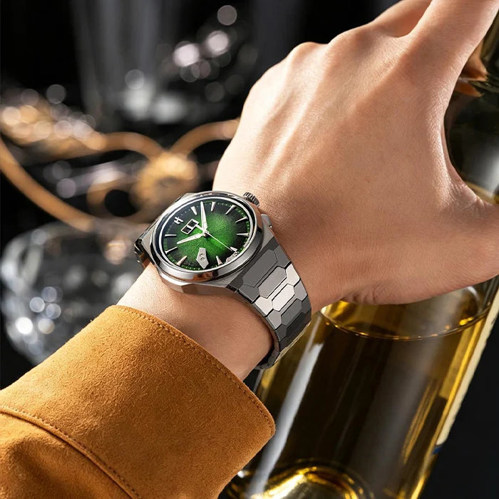 A close-up lifestyle shot of a man's hand wearing a silver-toned smartwatch with a green glowing face and metallic link band, resting near a gold bottle against a dark, blurred background.