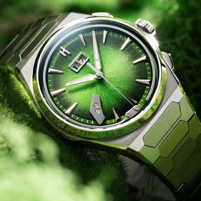 A close-up of a wristwatch with a metallic silver-toned case and green gradient dial, resting on a textured green surface.