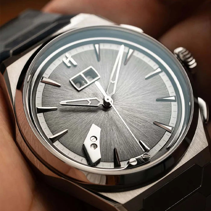 Close-up of a wristwatch with a silver-toned metal case, a gray sunburst dial, and a black strap, shown being worn on a person's wrist.
