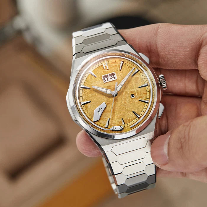 Silver and gold watch held in a hand with a blurred background