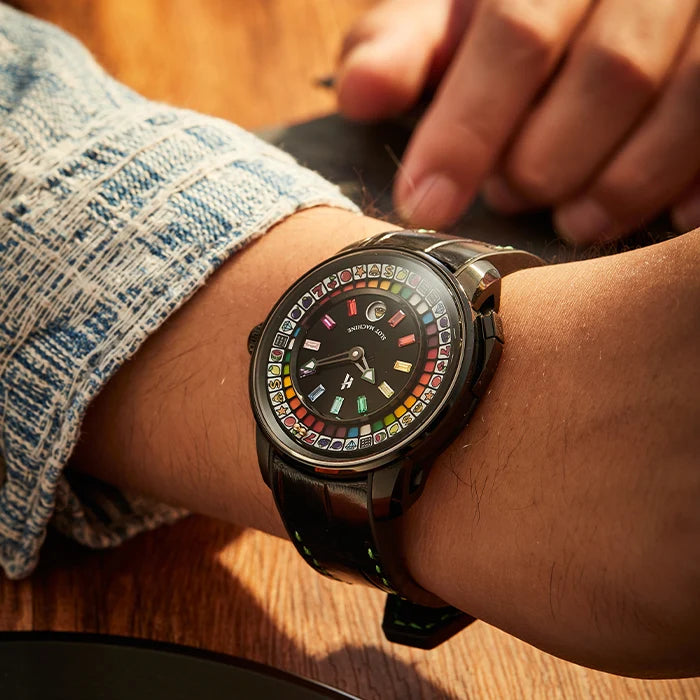 A close-up lifestyle shot of a smartwatch on a person's wrist, showing a colorful digital watch face with a black strap and a denim sleeve in the background.