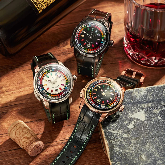 Three luxury wristwatches with colorful world map dials are arranged on a rustic wooden table with a wine bottle, a glass of red wine, a cork, and a book as styled props.