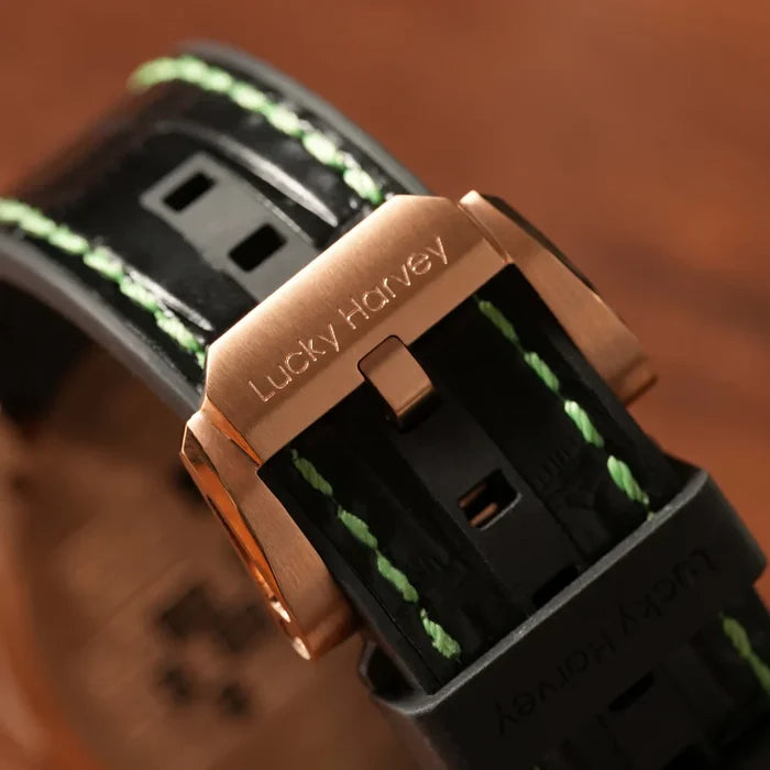 Close-up of a watch with a rose gold buckle and green stitching on a wooden surface.