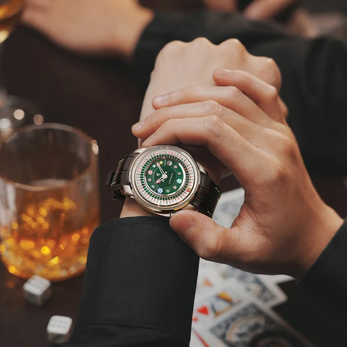 Hand wearing a watch with a green face, blurred bar setting with drinks and cards.