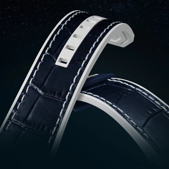 Close-up of a dark navy leather watch strap with white stitching and a white metal buckle, shown against a dark starry background.