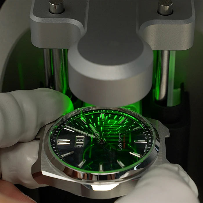 Watch with green face and silver case being held by a gloved hand.