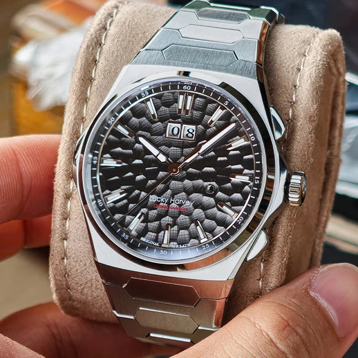A close-up of a Rock horo wristwatch with a textured dark gray dial and silver-toned case, resting on a beige suede-like display cushion held by hands.