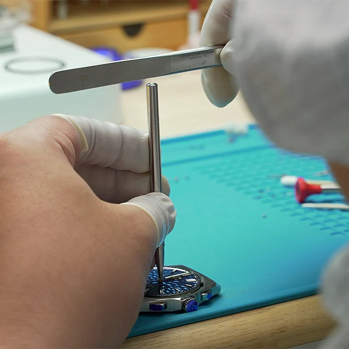 Person working on a watch with tools on a blue mat
