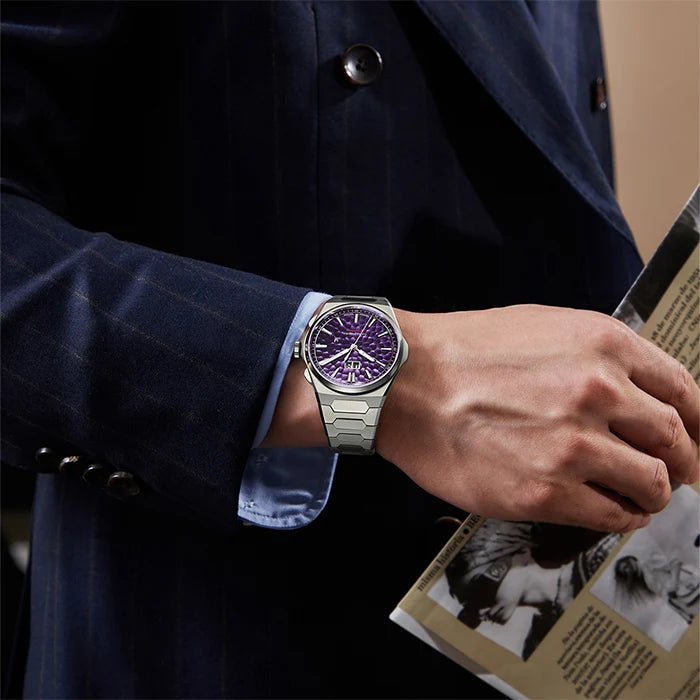 Person wearing a watch with a purple face, holding a book, dressed in a dark coat.