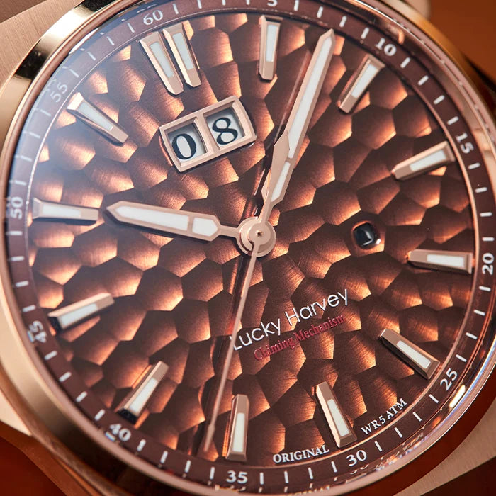 Close-up of a Lucky Harvey Commemoration watch dial with a textured bronze-brown honeycomb pattern, rose gold case, and date window.