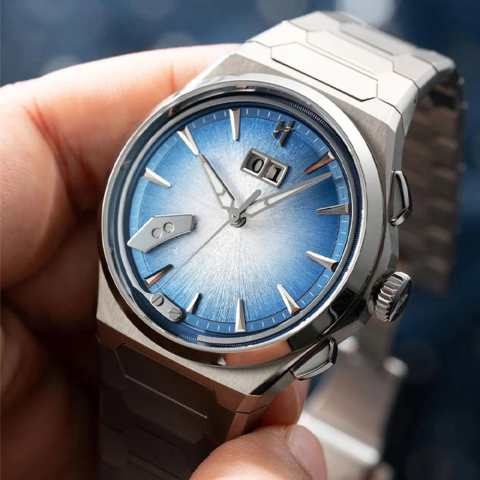 A close-up of a hand holding a stainless steel wristwatch with a blue sunburst dial and silver-toned metal bracelet.