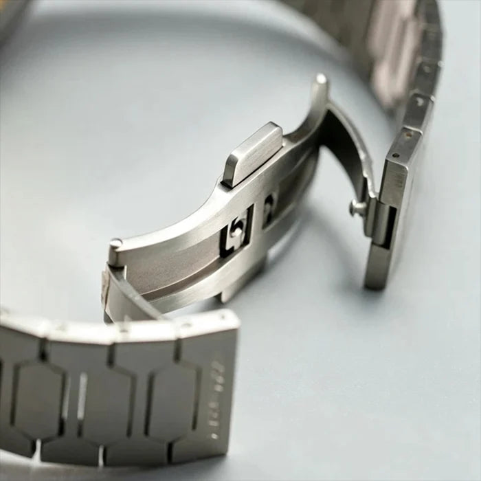 Close-up of a stainless steel watch band clasp and links on a light gray background.