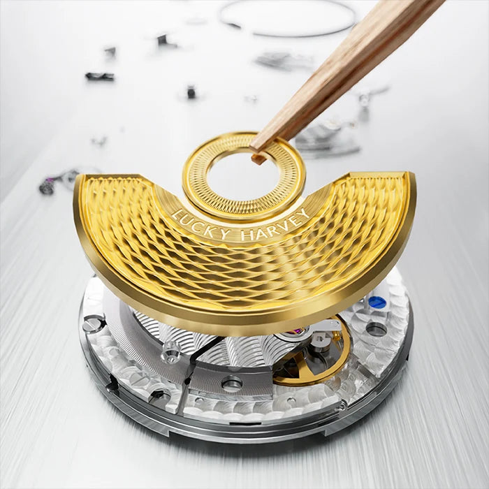 Close-up of a gold-toned watch component with a curved textured plate engraved with 'LUCKY HARVEY', held by wooden tweezers over an exposed mechanical movement on a light gray brushed surface.