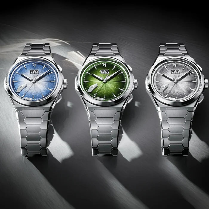 Three stainless steel wristwatches with hexagonal links are lined up on a dark metallic surface. The watches feature blue, green, and silver sunburst dials, each with a date window at 3 o'clock.