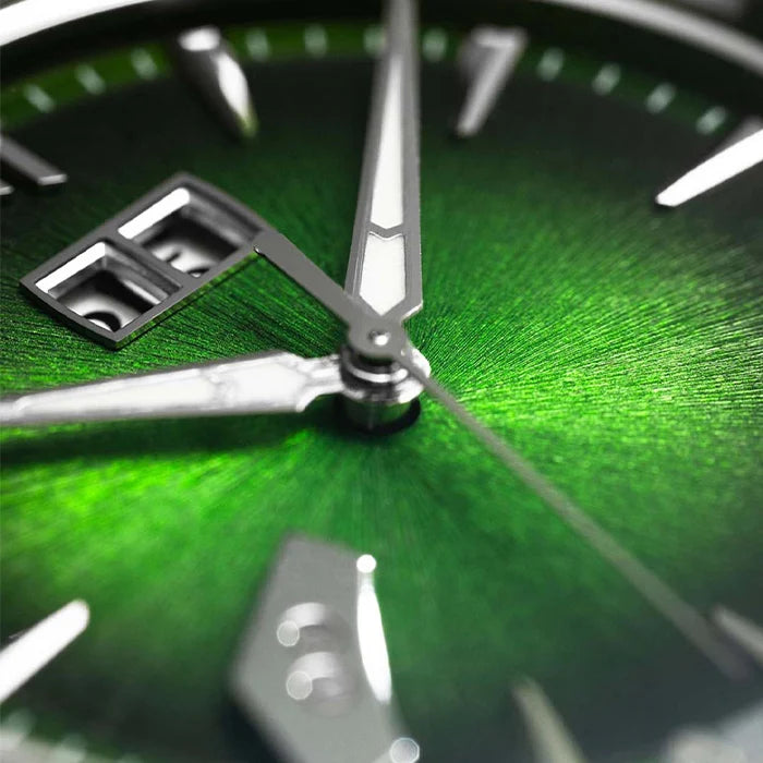 Close-up of a green analog watch face with silver hands and markers, showing a textured dial and polished metal details.