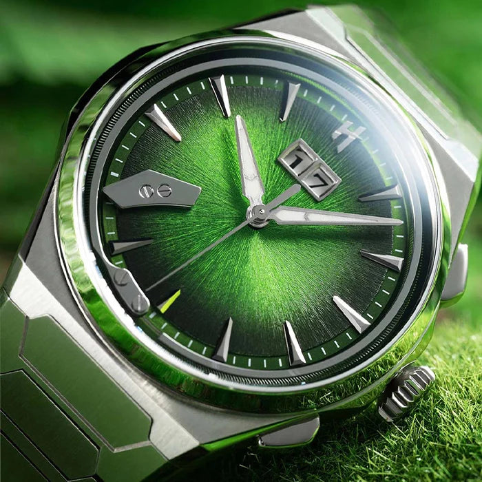 A close-up of a wristwatch with a metallic silver-toned case and green dial, resting on a green grass-like surface.