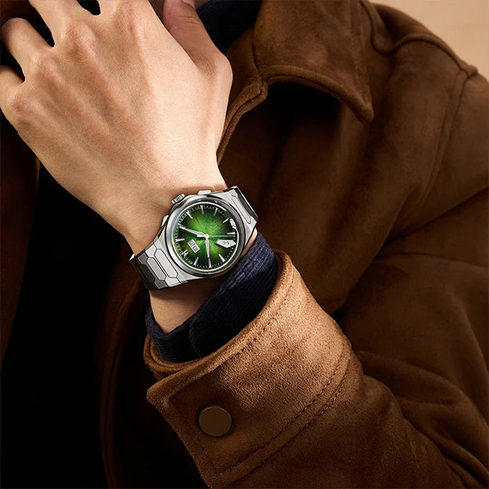 A close-up of a person's wrist wearing a silver-toned watch with a glowing green dial, styled with a brown suede jacket.