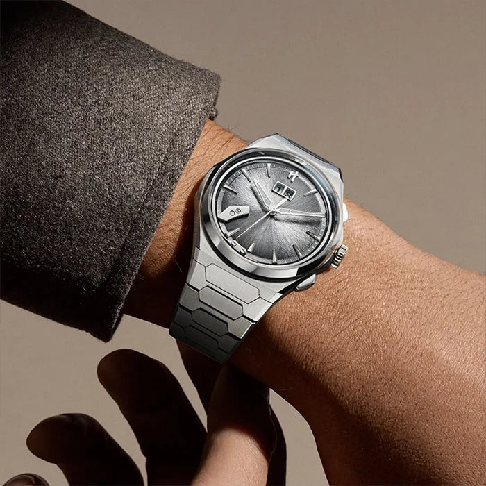 A silver-toned titanium  wristwatch with a textured dial and integrated metal bracelet, shown worn on a person's wrist with a dark gray sleeve visible.