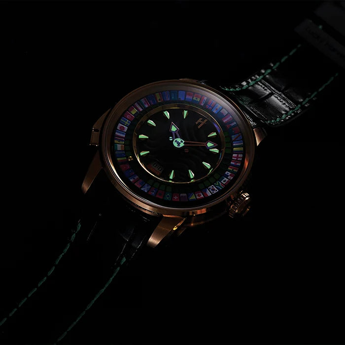 A wristwatch with a dark rose gold-toned case, a glowing green and multicolor dial, and a black leather strap with green stitching, photographed against a solid black background.