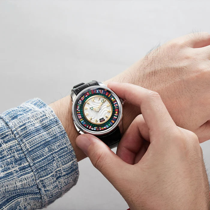 A close-up lifestyle shot of a person's hands adjusting a novelty watch on their wrist. The watch features a black strap, a silver-toned case, and a dial decorated with various colorful international flags.