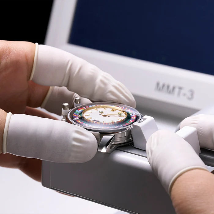 Person wearing white gloves adjusting a colorful watch under a light source